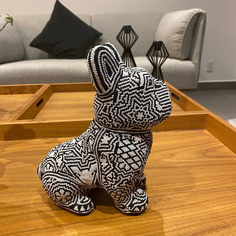 May include: A black and white beaded figurine of a French bulldog. The figurine is sitting on a wooden table.
