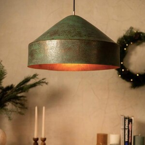 May include: A green hammered metal pendant light fixture with a copper interior. The light is hanging from a ceiling and is illuminating the room.
