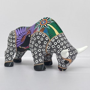 May include: A black and white ceramic bull figurine with colorful painted details, including a purple bird with a black head and a green and yellow flower on the back.
