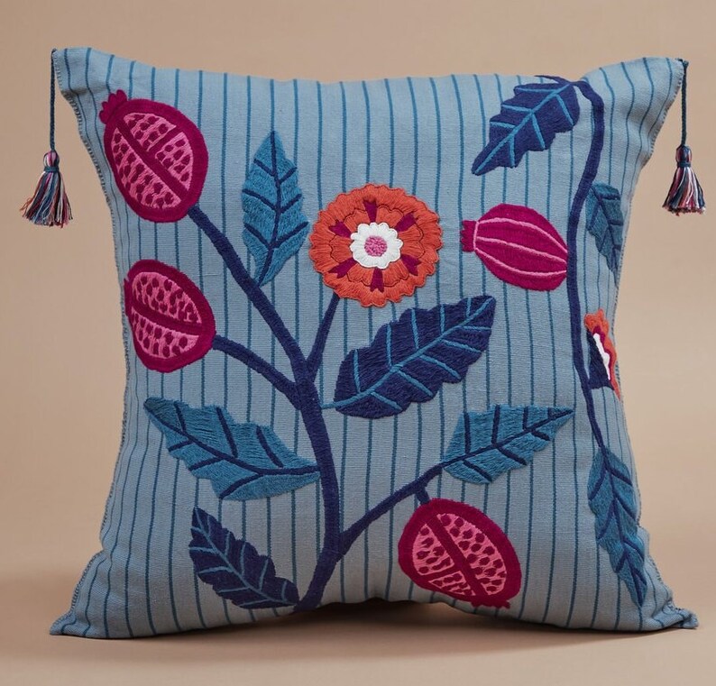 May include: A blue and white striped pillow with embroidered flowers and leaves in shades of pink, red, and orange.