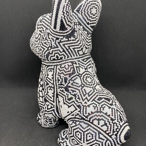 May include: A black and white ceramic figurine of a dog with a geometric pattern. The figurine is sitting on a black surface.