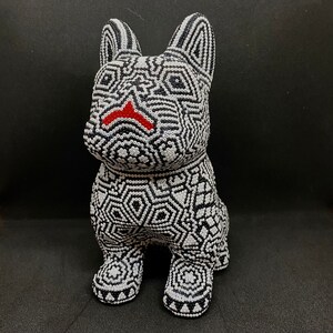 May include: A black and white beaded figurine of a dog. The dog is sitting with its legs crossed and has a red nose.