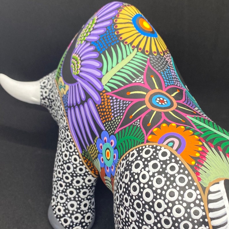 May include: A black ceramic bull figurine with a white horn, painted with colorful flowers and a polka dot pattern.