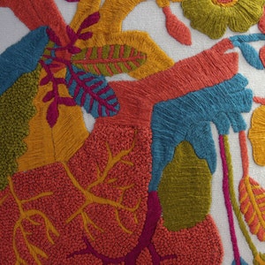 May include: A white pillow with colorful embroidered flowers and leaves. The flowers are yellow, orange, pink, and red. The leaves are green and yellow. The embroidery is done in a variety of stitches, including satin stitch, French knots, and seed stitch.