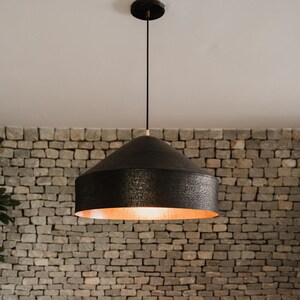 May include: A black pendant light with a hammered copper finish hangs from a white ceiling against a brick wall.