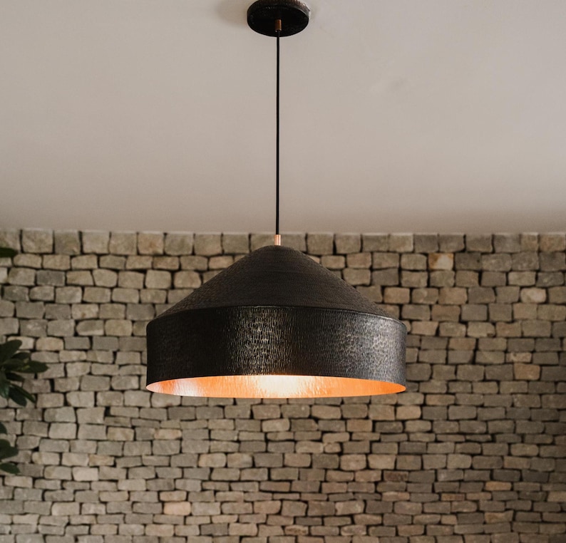 May include: A black pendant light with a hammered copper finish hangs from a white ceiling against a brick wall.