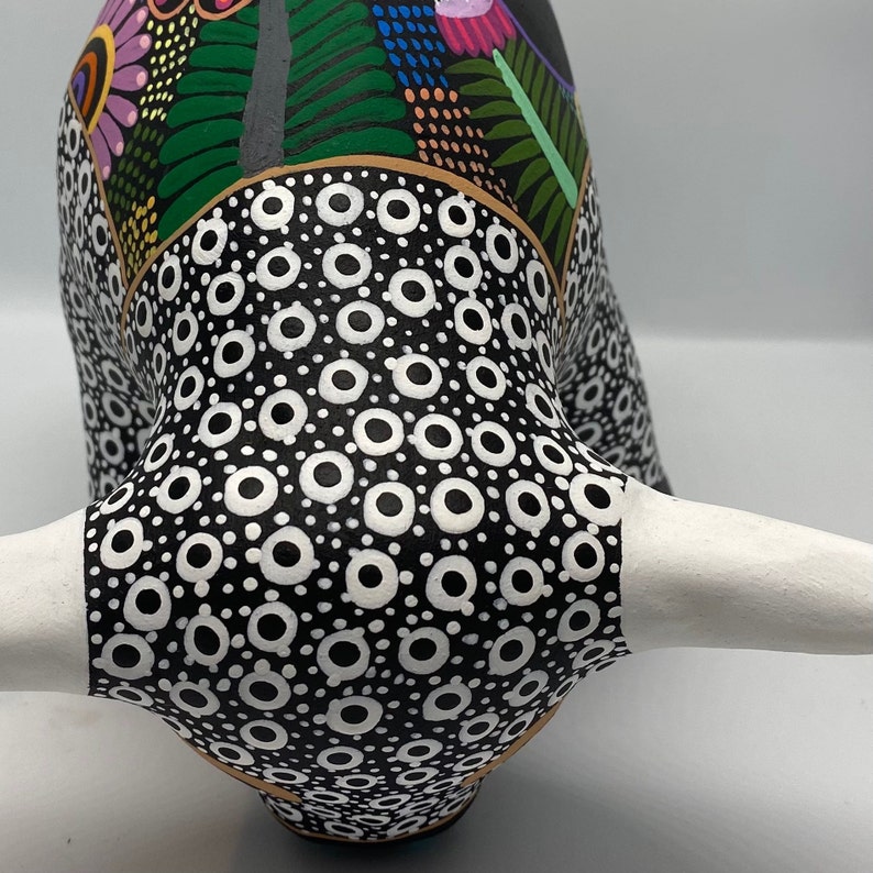 May include: A black and white ceramic bull figurine with a colorful floral pattern on the head and horns. The bull has a white horn and a black and white polka dot pattern on the body.