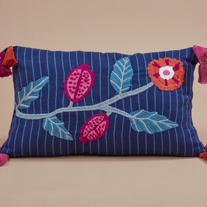 May include: Blue and white striped pillow with embroidered pink and red flowers and leaves. The pillow has tassels on each end.