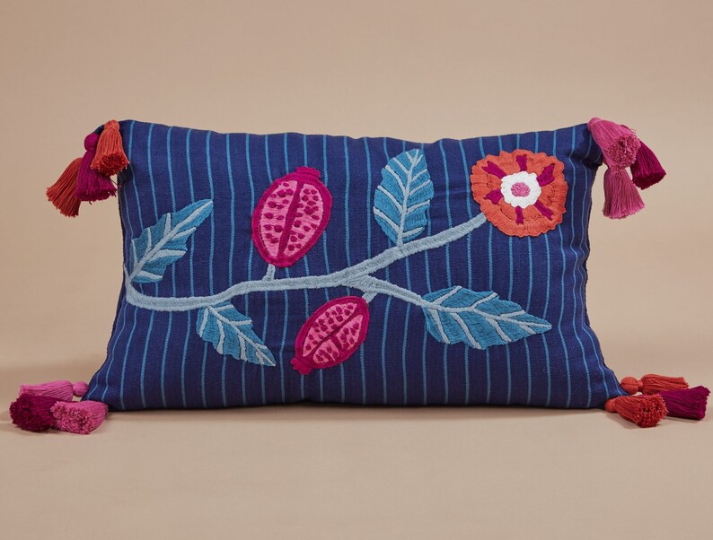 May include: Blue and white striped pillow with embroidered pink and red flowers and leaves. The pillow has tassels on each end.