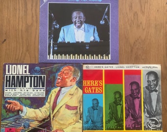 Pode incluir: Três discos de vinil vintage de Lionel Hampton. O primeiro disco é intitulado "Hamp The Champ" e apresenta uma foto de Lionel Hampton tocando vibrafone. O segundo disco é intitulado "Plays Vibes with His Band" e apresenta uma foto de Lionel Hampton tocando vibrafone. O terceiro disco é intitulado "Here's Gates" e apresenta uma foto de Lionel Hampton tocando vibrafone.