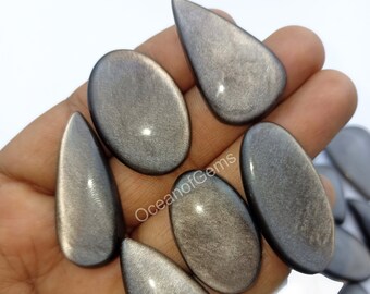 Könnte beinhalten: Eine Sammlung von sieben silbernen und grauen Edelstein-Cabochons in Tropfenform. Die Steine haben eine schimmernde, irisierende Oberfläche.