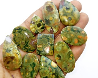 May include: A collection of ten green, brown, and orange ocean jasper cabochons in various shapes, including oval, teardrop, and square. The cabochons are polished and have a smooth, glossy finish.