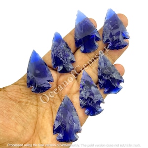 May include: Seven blue glass arrowheads with a carved design. The arrowheads are arranged in a hand, with the points facing upwards.