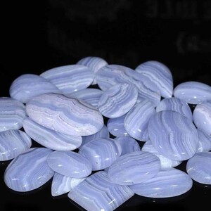 May include: A collection of blue agate cabochons, featuring a variety of shapes and sizes. The stones have a banded pattern of light and dark blue.