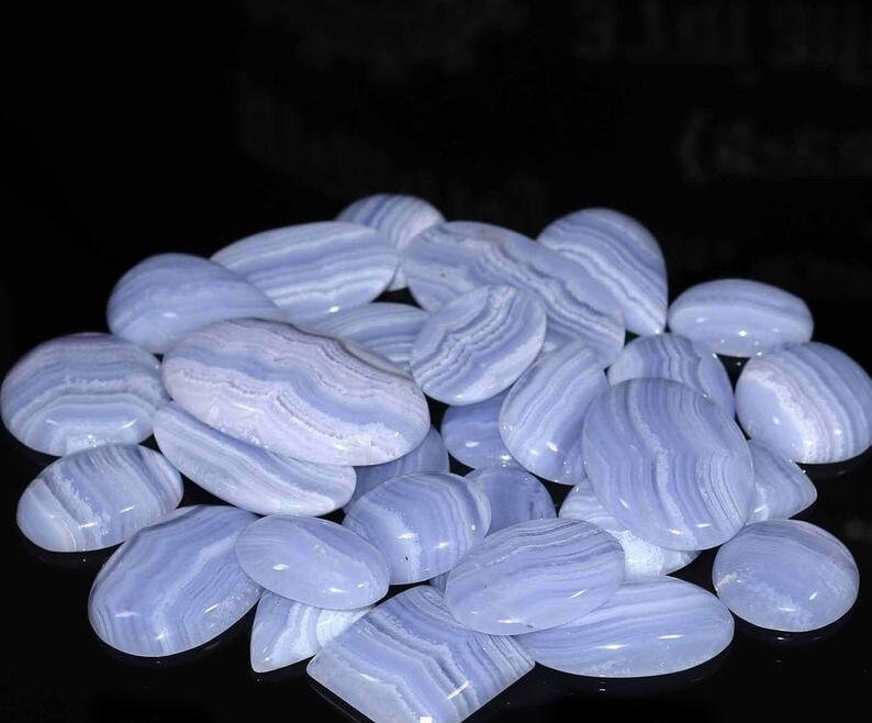 May include: A collection of blue agate cabochons, featuring a variety of shapes and sizes. The stones have a banded pattern of light and dark blue.