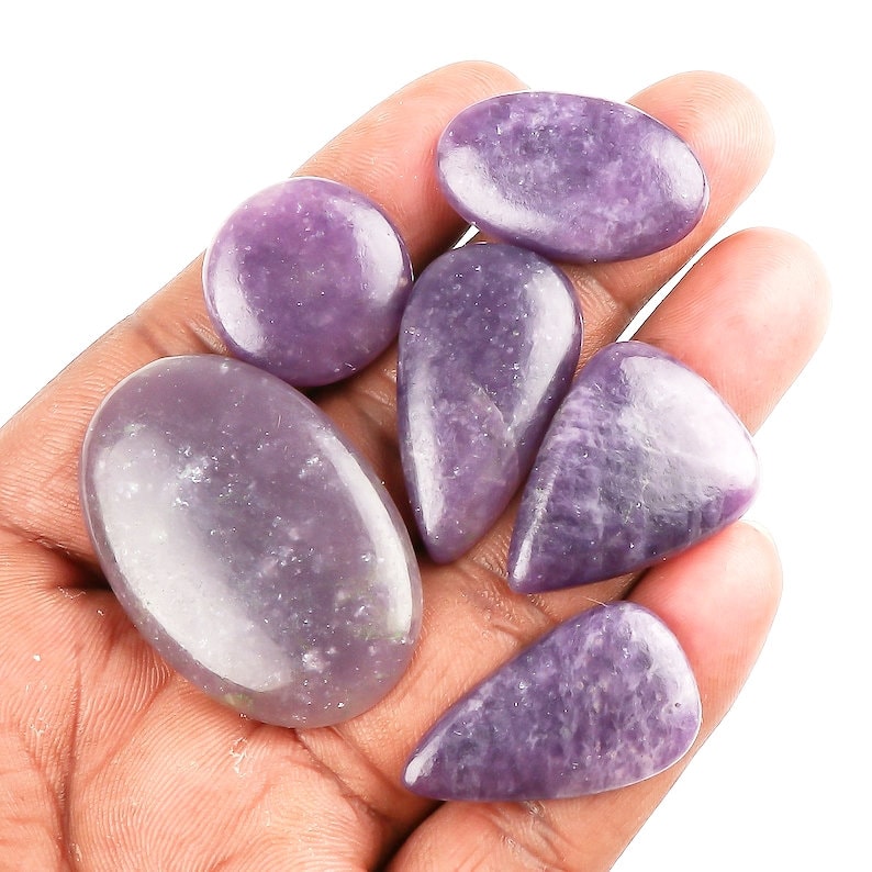 May include: A collection of six purple lepidolite cabochons, some oval shaped and some teardrop shaped, in various sizes.