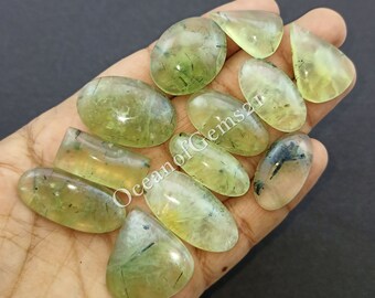 May include: A collection of ten green and clear gemstone cabochons with black inclusions. The cabochons are oval, teardrop, and rectangular shapes.