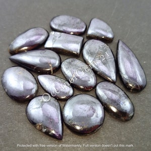 K&ouml;nnte beinhalten: Eine Sammlung von 12 regenbogenfarbenen schwarzen Edelstein-Cabochons in verschiedenen Formen, darunter Tropfen, Oval und Rechteck. Die Steine haben eine schimmernde, metallische Oberfl&auml;che.