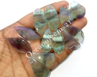 Può includere: Una collezione di dieci cabochon di fluorite a forma di lacrima, di colore verde, viola e bianco. I cabochon sono lisci e lucidi.