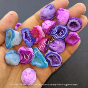 May include: A collection of 12 small, colourful agate crystals with a variety of purple, pink, blue, and white hues. The crystals have a natural, rough texture and a hollow centre.