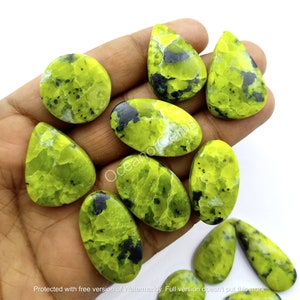 Pode incluir: Uma coleção de dez pedras preciosas cabochão verdes e pretas, algumas ovais e outras em forma de lágrima, em uma mão.