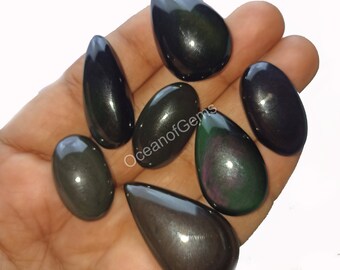Könnte beinhalten: Sieben schwarze Obsidian-Cabochons mit irisierenden Regenbogen-Schimmern. Die Cabochons sind tropfenförmig und haben eine glatte, polierte Oberfläche.