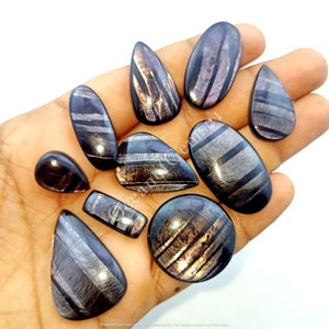 Puede incluir: Una colección de 10 cabujones de piedra preciosa con un patrón de rayas negras y plateadas. Los cabujones son de varias formas y tamaños, incluyendo ovalados, redondos y en forma de lágrima.