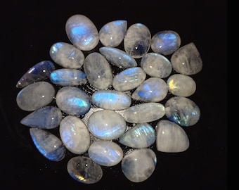 May include: A collection of iridescent moonstone cabochons in various shapes and sizes. The stones are a milky white color with a blue sheen.