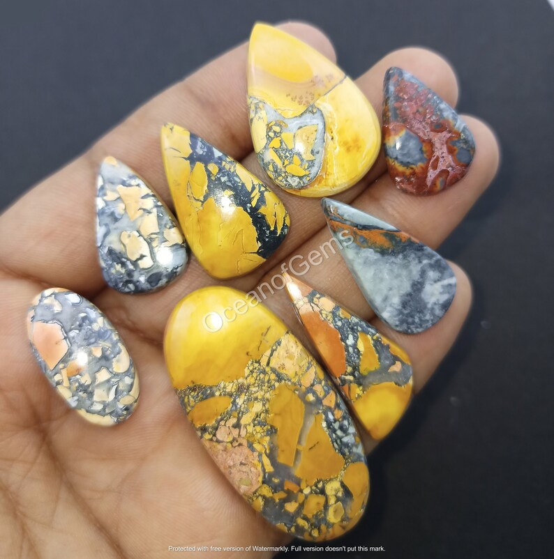 Puede incluir: Una colecci&oacute;n de ocho cabujones de piedra preciosa de color amarillo, naranja y gris con un patr&oacute;n moteado. Los cabujones tienen varias formas, incluyendo la forma de l&aacute;grima y ovalada.