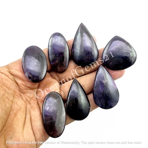 May include: Seven iridescent purple and black gemstone cabochons in various teardrop and oval shapes. The stones are smooth and polished, with a shimmering, metallic finish.