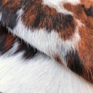 Peut inclure: Gros plan sur une peau de vache avec un motif naturel. La peau présente un mélange de taches marron, noires et blanches, avec une surface douce et texturée. Les couleurs et les motifs créent une esthétique rustique unique, adaptée à la décoration intérieure.
