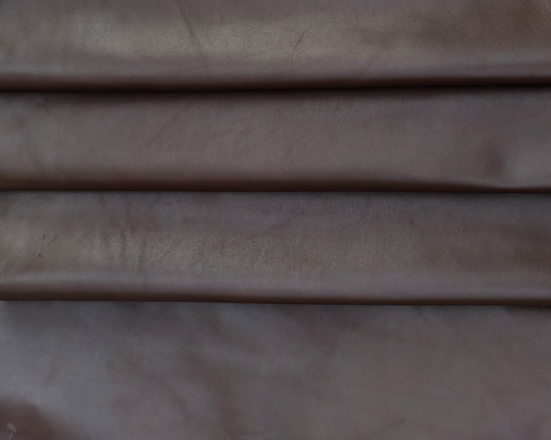 May include: Close-up of a folded piece of brown leather. The leather has a smooth, slightly shiny surface.