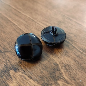 Può includere: Due bottoni in pelle nera con un design cucito. Un bottone ha un anello nella parte superiore.