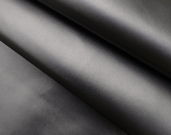 May include: Close-up of a black leather fabric with a smooth, slightly textured surface. The fabric is folded in half, showing the texture and sheen.