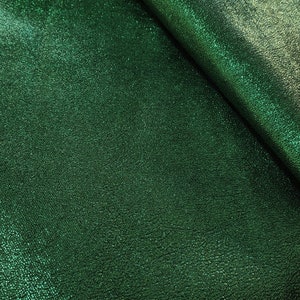 Puede incluir: Primer plano de una tela verde esmeralda texturizada con un sutil brillo met&aacute;lico. El material est&aacute; doblado, revelando un juego de luces y sombras en su superficie. La textura de la tela parece ligeramente en relieve, d&aacute;ndole un aspecto t&aacute;ctil.