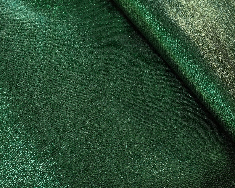 Puede incluir: Primer plano de una tela verde esmeralda texturizada con un sutil brillo met&aacute;lico. El material est&aacute; doblado, revelando un juego de luces y sombras en su superficie. La textura de la tela parece ligeramente en relieve, d&aacute;ndole un aspecto t&aacute;ctil.