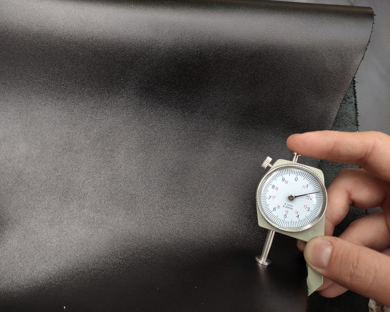Op de afbeelding: Close-up van een zwart lederen materiaal met een meter die een dikte van 1,7 mm meet.