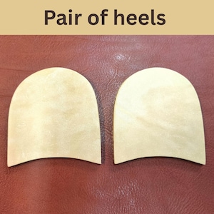 May include: Two wooden shoe heels with a light tan color. The heels are arched and have a smooth surface. The text "Pair of heels" is at the top of the image. The background is a reddish-brown leather.