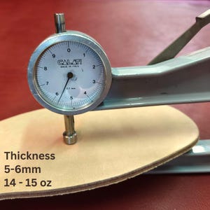 May include: A dial caliper measuring the thickness of a piece of light brown leather. The text on the image reads "Thickness 5-6mm 14-15 oz". The caliper is labeled "CALATI MADE IN ITALY".