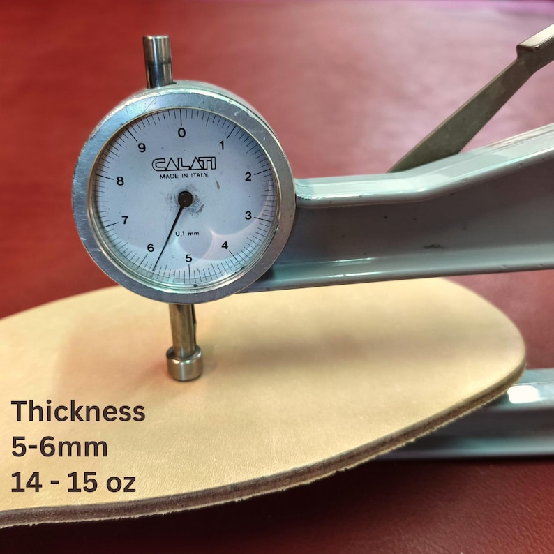 May include: A dial caliper measuring the thickness of a piece of light brown leather. The text on the image reads "Thickness 5-6mm 14-15 oz". The caliper is labeled "CALATI MADE IN ITALY".