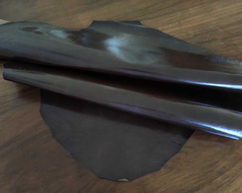 May include: A piece of dark brown leather with a glossy finish. The leather is folded in half and appears to be soft and supple.
