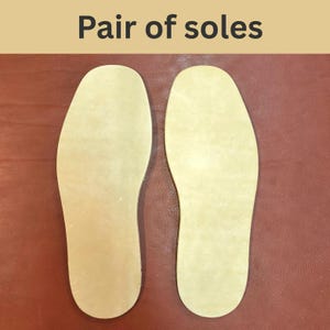 May include: A pair of light beige shoe soles, with the text "Pair of soles" at the top. The soles are placed on a reddish-brown surface. The soles are shaped to fit the bottom of a foot.