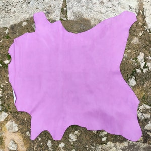 Pode incluir: Uma grande peça de couro roxo claro colocada sobre uma superfície áspera, cinza e texturizada.