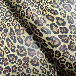 Puede incluir: Primer plano de una tela con estampado de leopardo. La tela es de color beige claro con manchas marrones y negras.