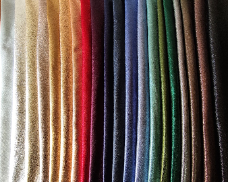 Puede incluir: Una colecci&oacute;n de muestras de tela en una variedad de colores, incluyendo blanco, dorado, rojo, azul marino y verde. La tela tiene un brillo sutil, y los pliegues crean sombras que resaltan los diferentes tonos. La disposici&oacute;n muestra la gama de colores disponibles.