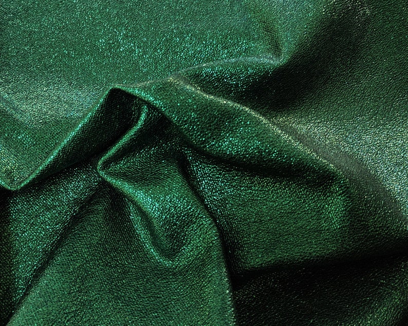 Emerald green metallic leather with a denim textured surface. The leather is folded and draped, showing the softness and the shimmery effect of the material.