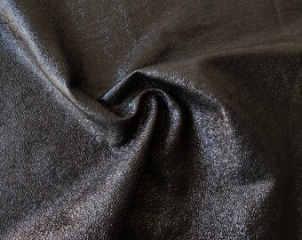 May include: Close-up of black leather fabric with a textured surface. The fabric is folded and has a slight sheen.