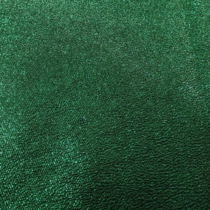 Puede incluir: Primer plano de una superficie texturizada de color verde esmeralda. El material tiene un brillo sutil, con una textura ligeramente rugosa e irregular. El color es un verde intenso y rico, con variaciones de tono.