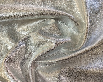 May include: Silver metallic fabric with a textured surface. The fabric is wrinkled and folded, showing the shimmery effect of the material.