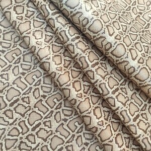 Peut inclure: Gros plan sur un tissu beige avec un motif de peau de serpent brun. Le tissu est plié et texturé.